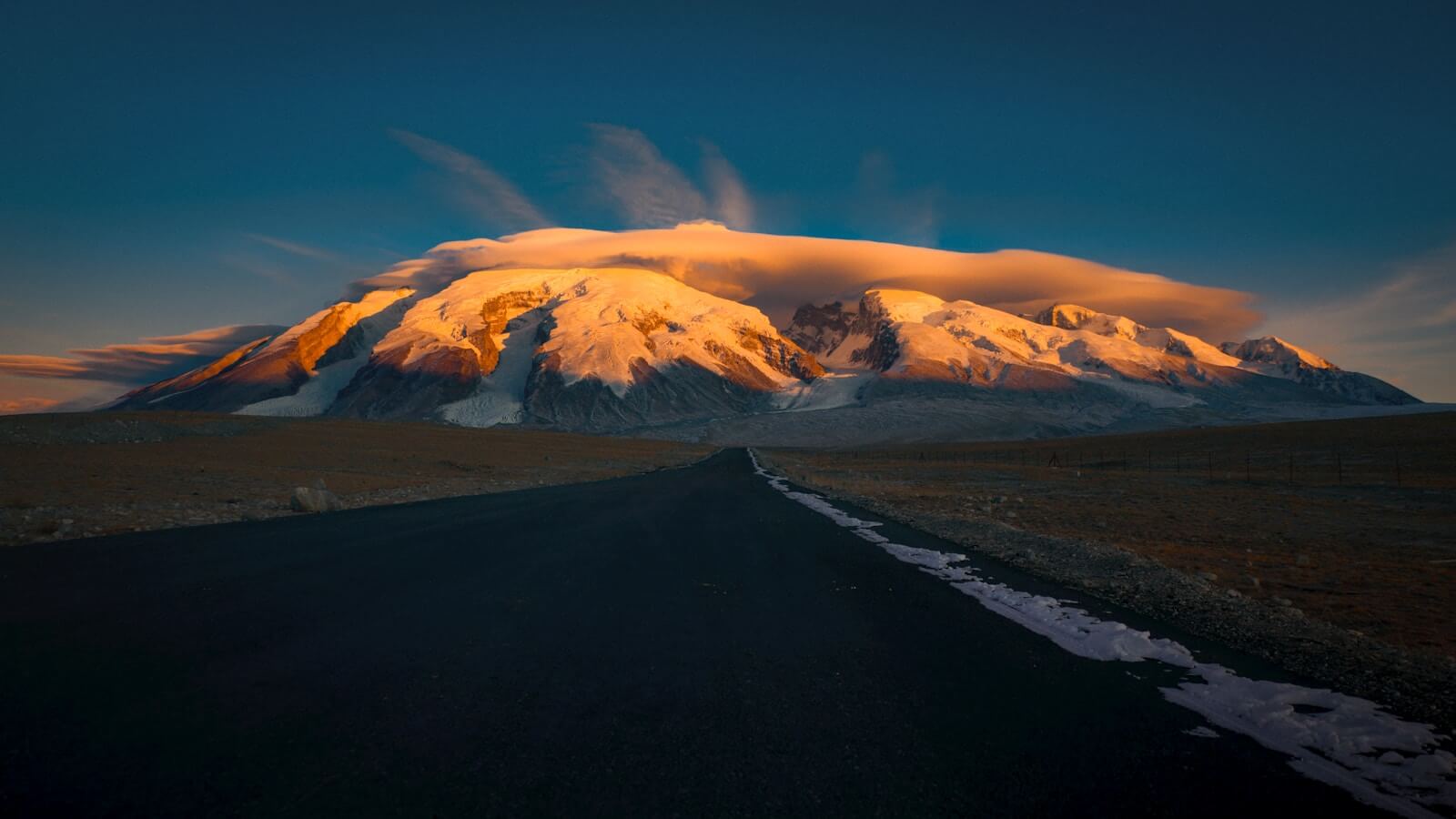 Snow-capped mountain illuminated by sunset with road.